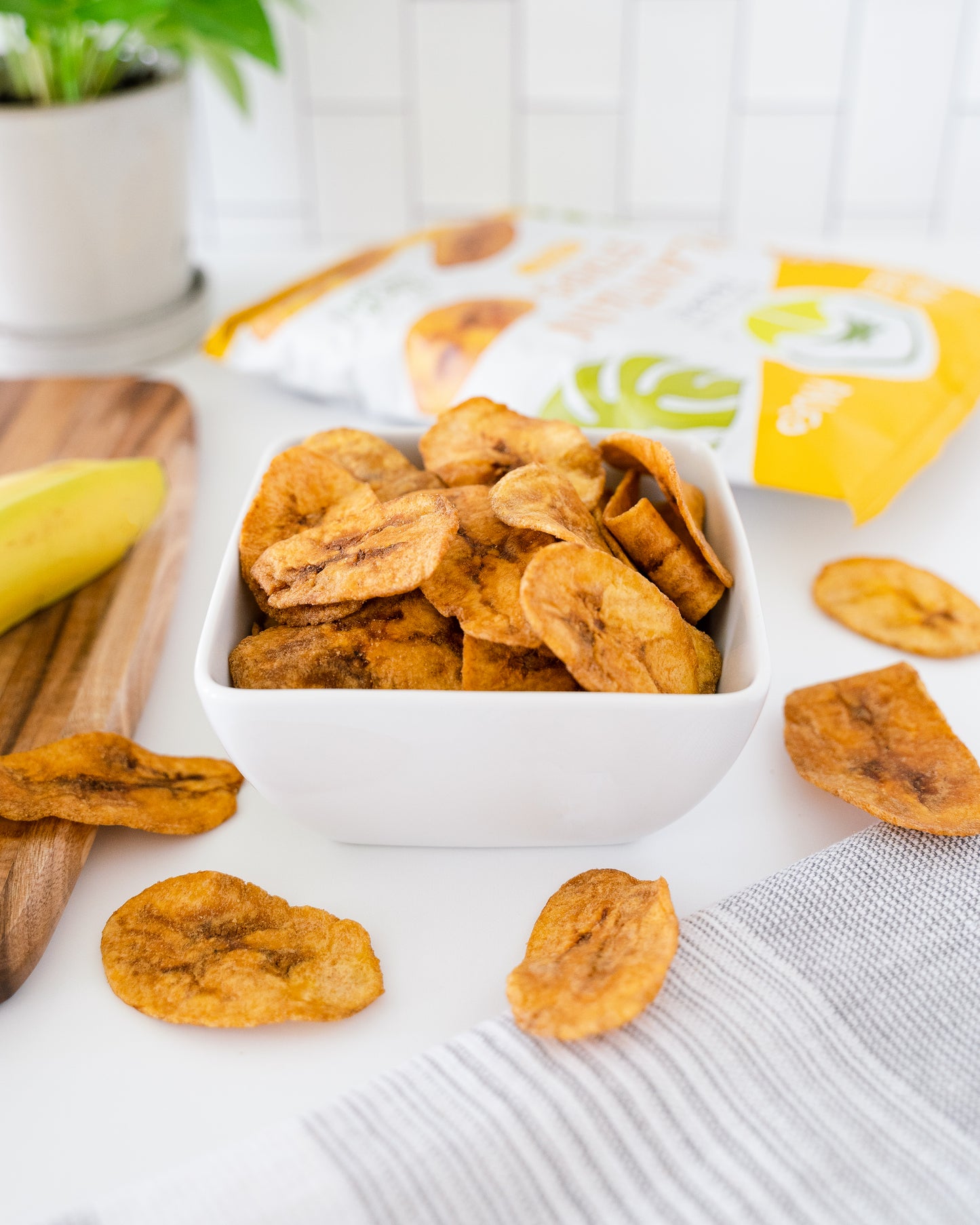 Dried banana chips in a white bowl with a yellow package in the background.